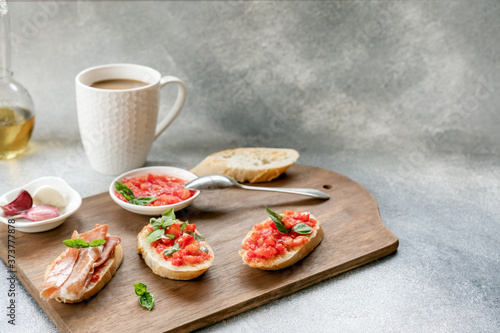 bruschetta, toast with sliced tomatoes, jamon and Basil on a wooden cutting Board and coffee with milk in a white Cup. copy space