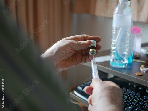 An old man's hands carefully pulling the medicine into the syringe by himself at home - self injecting in the elderly