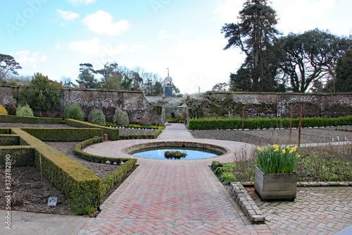 A formal garden in England with a round pond surrounded by brick pavers