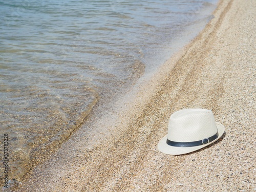 A white straw hat lies on the sand by the water. Sea beach on a summer sunny day. Sea vacation concept. Copy space. High quality photo