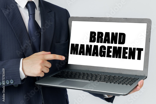 A businessman holds a laptop in his hands and shows on the screen with the text - BRAND MANAGEMENT