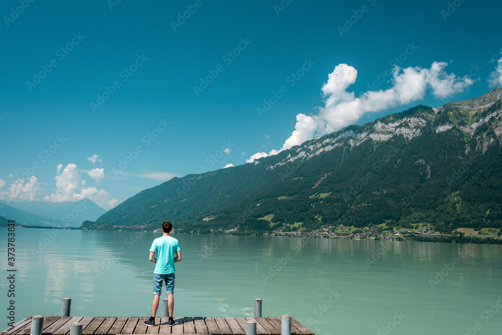 Traveler man standing on the lake wooden pier. Scenic views of the lake and rocky coast