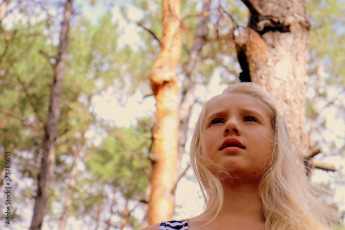 Girl with long blond hair portrait on a summer day against the background of the forest.