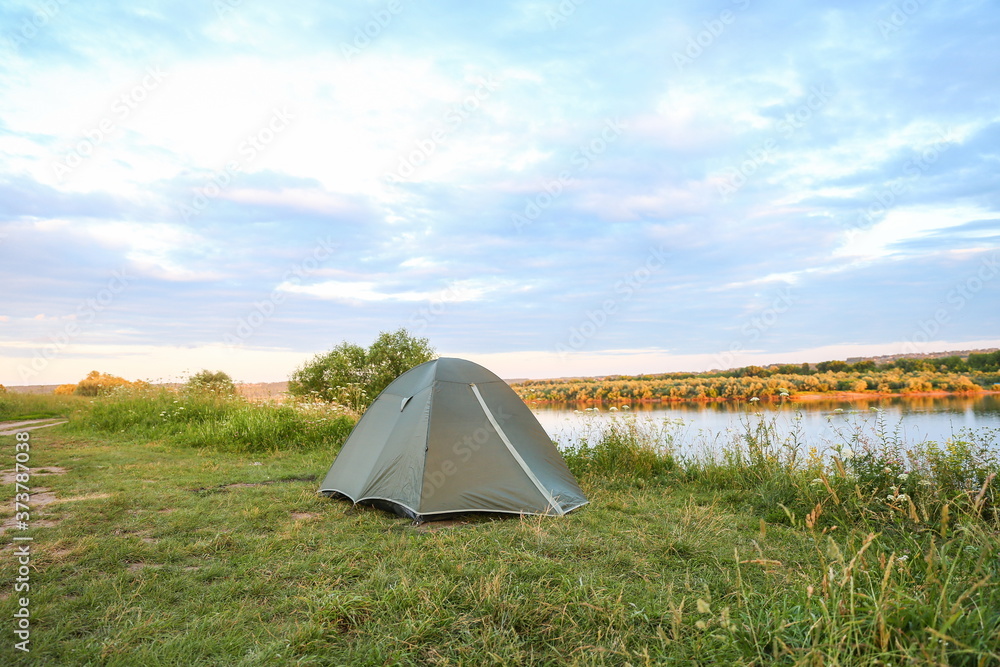 green tourist double tent is on the bank of the river at sunset