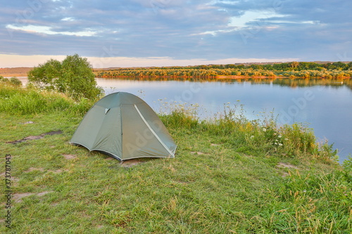 green tourist double tent is on the bank of the river at sunset