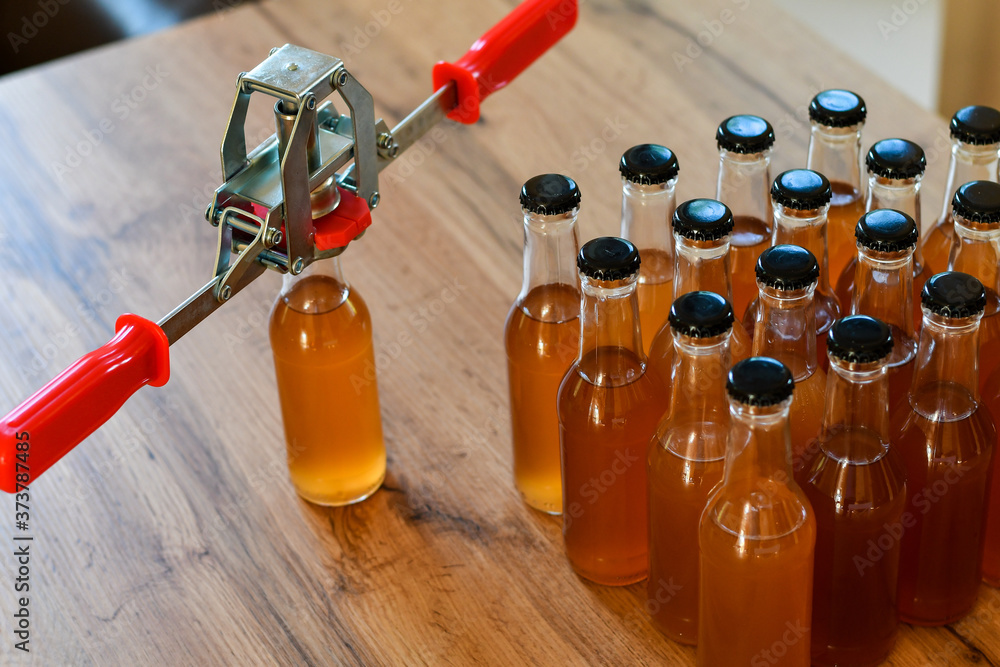 Naklejka premium Using hand capper for home brewing. Background of brown bottles with homemade liquor or alcohol. Selective focus.
