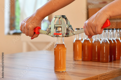 Using hand capper for home brewing. Background of brown bottles with homemade liquor or alcohol. Selective focus.