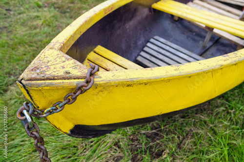 An old green wooden boat chained up on the lake shore in summertime