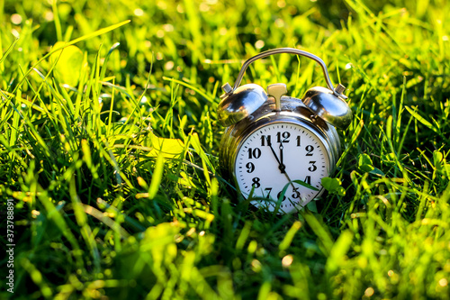 Conceptual alarm clock in fresh grass showing 5 minutes to 12, reminding that we have too little time to save our planet