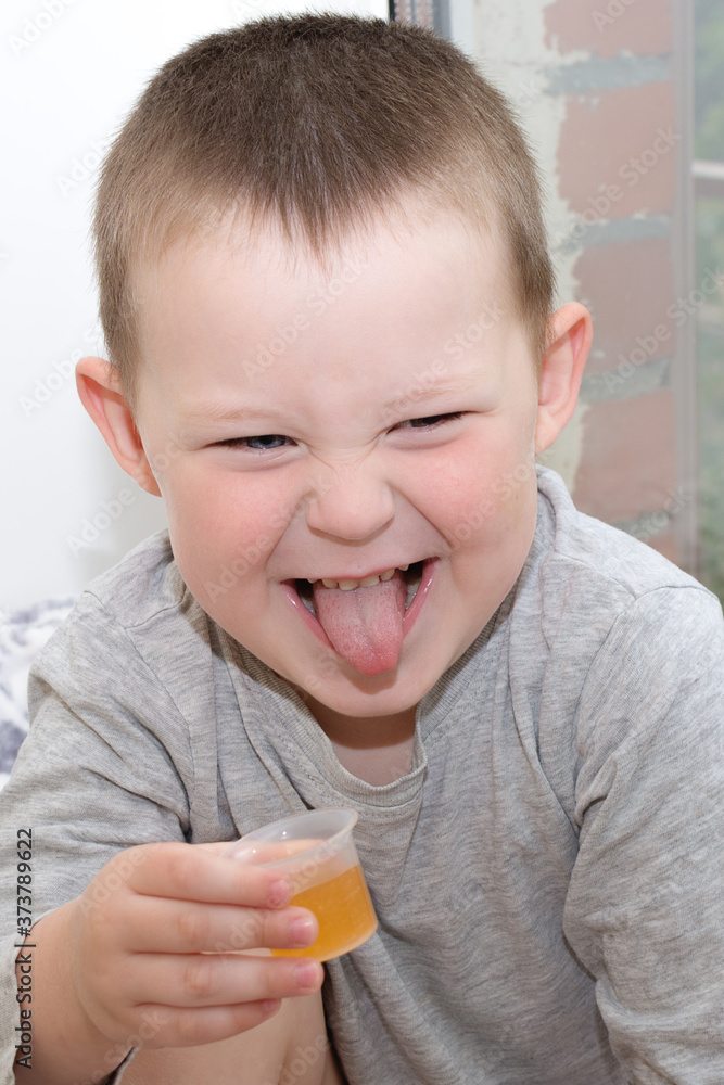 funny child holds a glass of medicine in his hands and makes faces with his tongue out. Idea - the child knows that the medicine is bitter, disgusting, tasteless and does not want to drink. funny child holds a glass of medicine in his hands and makes faces with his tongue out. Idea - the child knows that the medicine is bitter, disgusting, tasteless and does not want to drink.