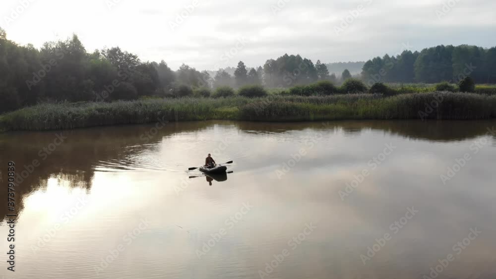 young stylish hipster fisherman sails in a boat on a lake or river between the reeds. A young man paddles on an inflatable boat. Relaxes in nature. camping by the water. Recreation young stylish hipster fisherman sails in a boat on a lake or river between the reeds. A young man paddles on an inflatable boat. Relaxes in nature. camping by the water. Recreation