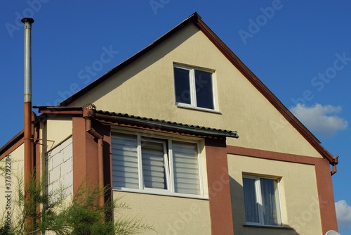 facade of a brown private house with white windows against a blue sky © butus