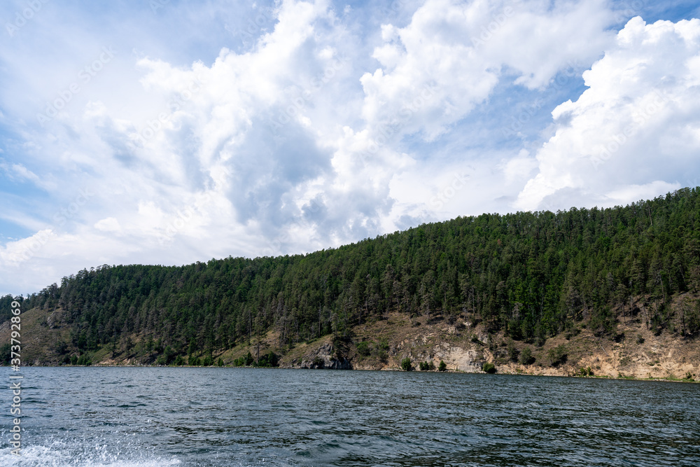 Russia, Irkutsk region, Baikal lake, July 2020: boast splash traces on water, cliffs and mountains in distance Russia, Irkutsk region, Baikal lake, July 2020: boast splash traces on water, cliffs and mountains in distance