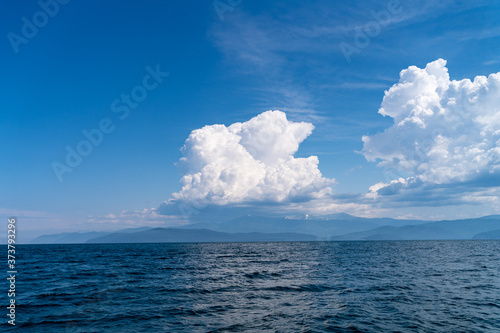 Russia, Irkutsk region, Baikal lake, July 2020: big white wooly soft cloud over smooth blue water