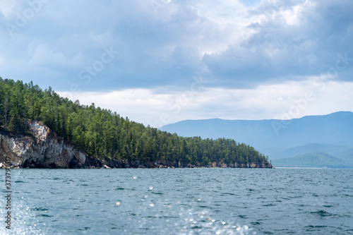 Russia, Irkutsk region, Baikal lake, July 2020: stone mountains with evergreen forest on them, from water view photo