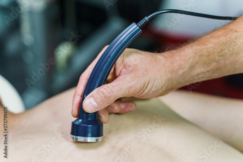 Close up on hand of unknown caucasian therapist holding ultrasonic ultrasound head transducer on skin of patient in treatment using medical equipment to reduce pain - healthcare and medicine concept