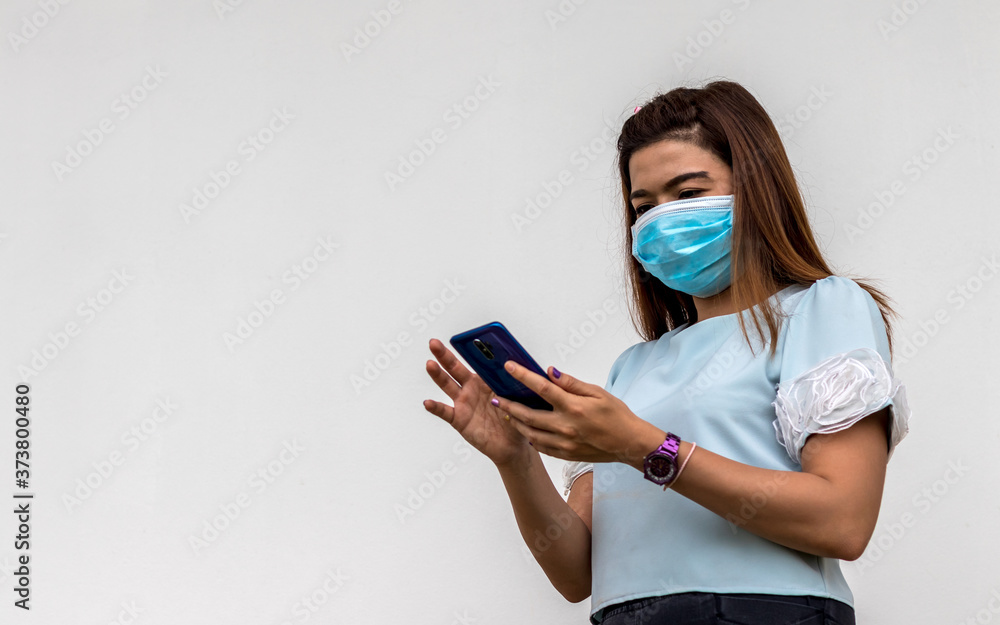A woman wearing a mask with a mobile phone near a concrete wall. A woman wearing a mask with a mobile phone near a concrete wall.