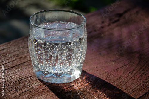 Φωτογραφία A glass with mineral, carbonated water on a wooden board in the garden