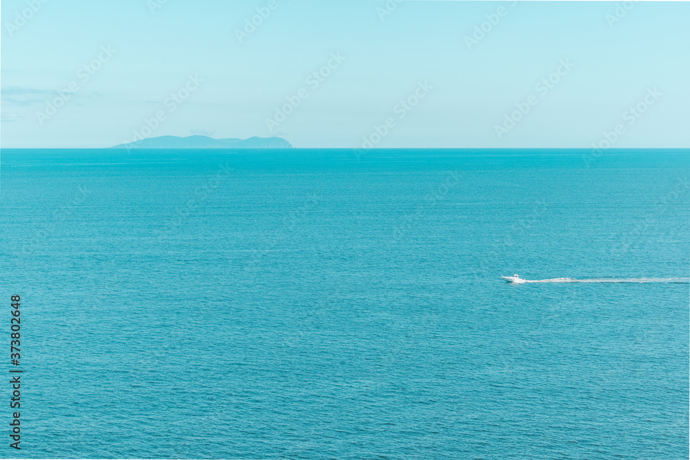 Blue clear sky and turquoise sea landscape. A boat floats in the distance. Summer sea bay. Vladivostok, Russian island, Chernyshev bay.