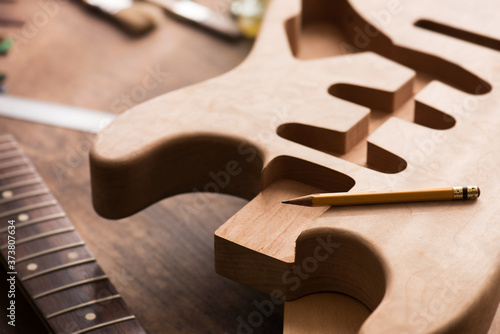 Electric guitar making. Guitar work shop. Unfinished solidbody electric guitar body on work bench. Focus is on pencil. Shallow depth of field.