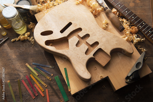 Guitar makers work table. Solid body electric guitar body and finishing materials and color test samples on a work bench.Intentionally shot with low key shadows and by the window type lighting.