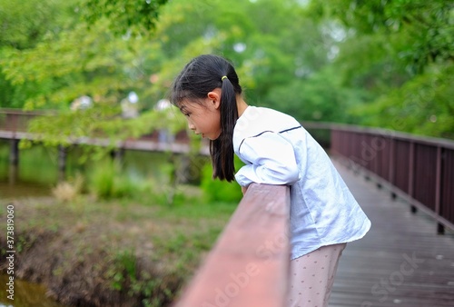 A cute young Asian girl leaning on the edge of a railing, looking down, sightseeing, feeling happy and smiling.