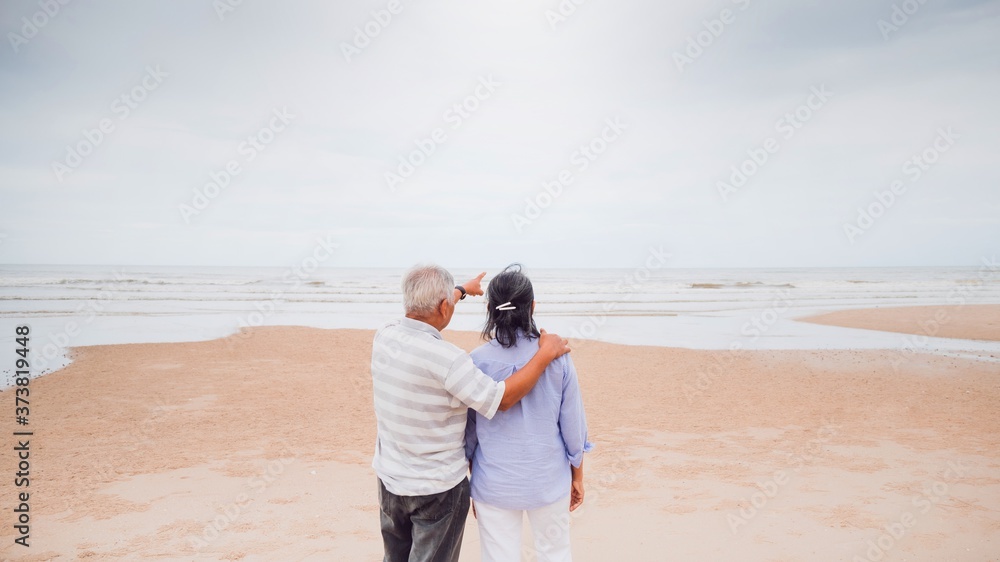 Asian old senior couples walking at the beach by the sea background on weekend vacation.Concept of happy living for the elderly.