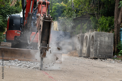 Hydraulic jackhammer from excavator construction truck drilling concrete ground with flying fragment concrete and dusty. Background for pm 2.5 micro dust problem and noise pollution or drainage system