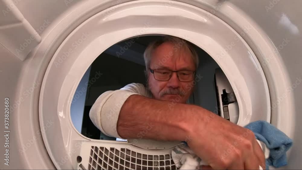 Senior man in a bad or angry mood removes laundry from dryer. Point of view from inside the dryer. Senior man in a bad or angry mood removes laundry from dryer. Point of view from inside the dryer.