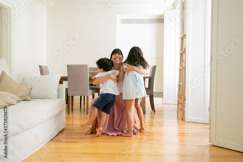 Laughing mother hugging adorable little kids at home. Happy pretty Caucasian mom embracing lovely children, smiling and playing with them. Motherhood, leisure and parenthood concept