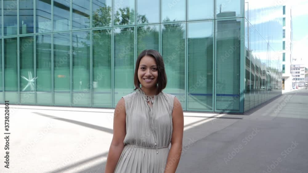 Elegant businesswoman is standing still in front of a tall glass-fronted office building. Slow motion dolly in shot Elegant businesswoman is standing still in front of a tall glass-fronted office building. Slow motion dolly in shot