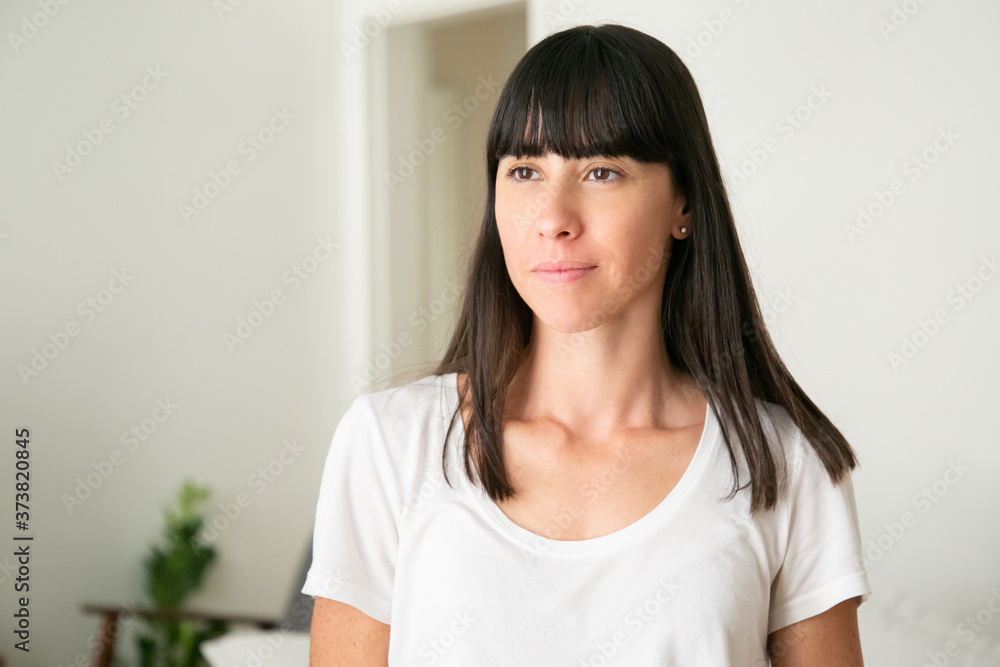 Portrait of pretty woman standing and looking away. Young confident lady posing in living room. Blurred background. Expression and appearance concept Portrait of pretty woman standing and looking away. Young confident lady posing in living room. Blurred background. Expression and appearance concept