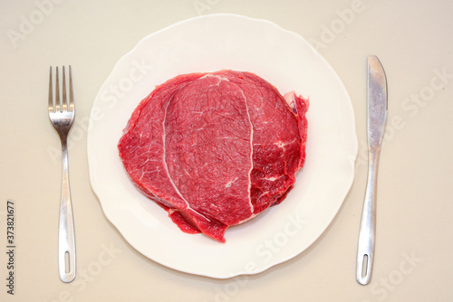 Raw beef meat steak with fork and knife on white plate on light background . Carnivore, keto