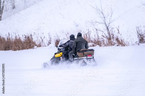 Two man on a snowmobile riding on the snow surface in the winter forest