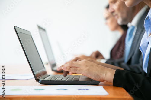Row of business people working at computers. Hands of employees typing on laptop keyboards. Side view, closeup, cropped shot. Communication or wireless technology concept
