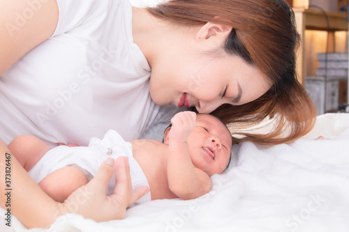 Beautiful happy Asian women mom kissing healthy toddler newborn baby in bed at home, Healthcare medical lifestyle mother's day/ young motherhood concept, infant sleep safe and protection in mom's arm