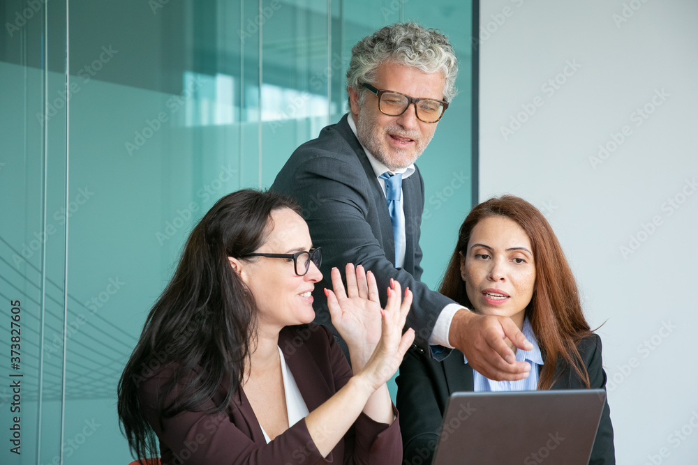 Business team watching and discussing presentation on laptop, male executive pointing at display, while female managers explaining details. Medium shot. Communication and teamwork concept Business team watching and discussing presentation on laptop, male executive pointing at display, while female managers explaining details. Medium shot. Communication and teamwork concept