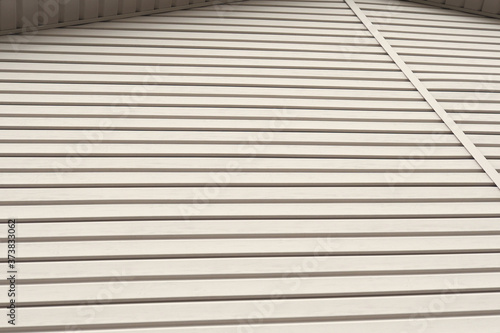The striped surface of the plastic siding and a piece of cornice. Construction and repair of buildings. Light brown or beige background or wallpaper. Building material and technologies