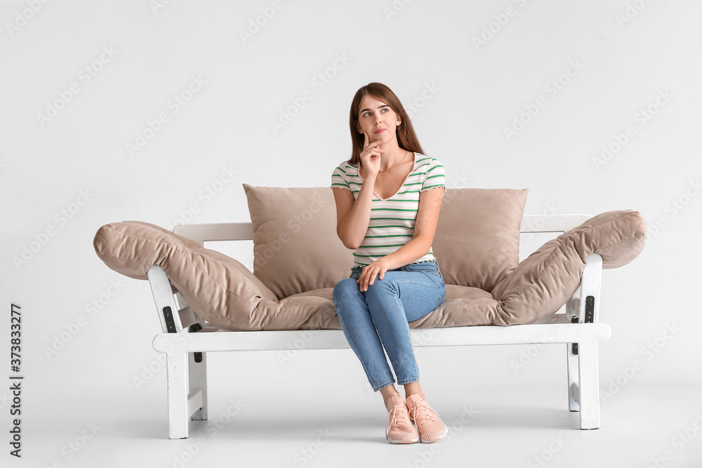 Thoughtful young woman on modern sofa against light background Thoughtful young woman on modern sofa against light background
