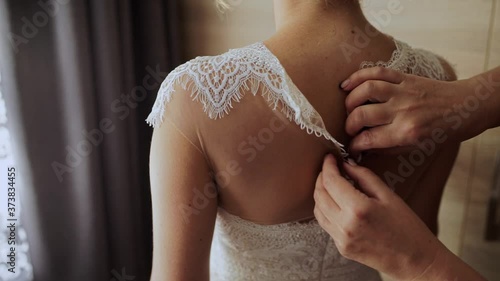bride buttoning wedding dress on the back photo