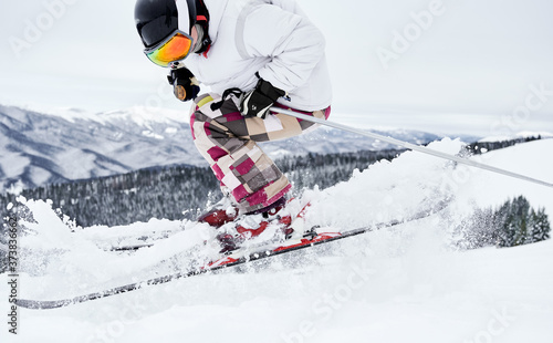 Male skier skiing on fresh powder snow with beautiful winter mountains on background. Man freerider making jump while sliding down snow-covered slopes. Concept of winter sports and ski resort.