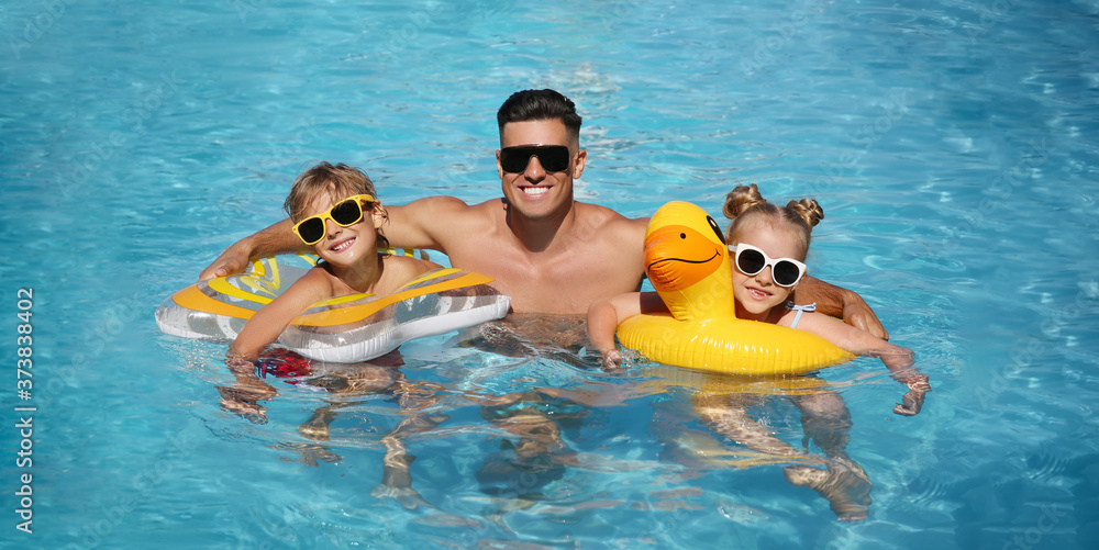 Happy man and his children with inflatable rings in outdoor swimming pool on sunny summer day