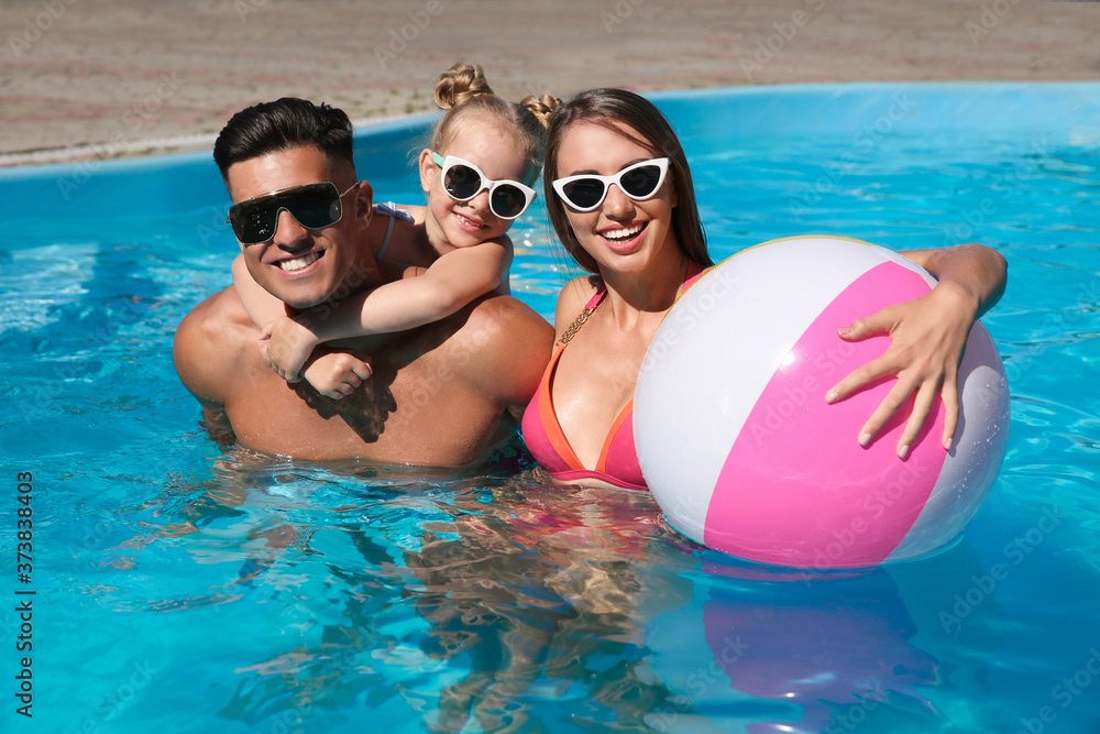 Happy family with inflatable ball in outdoor swimming pool on sunny summer day