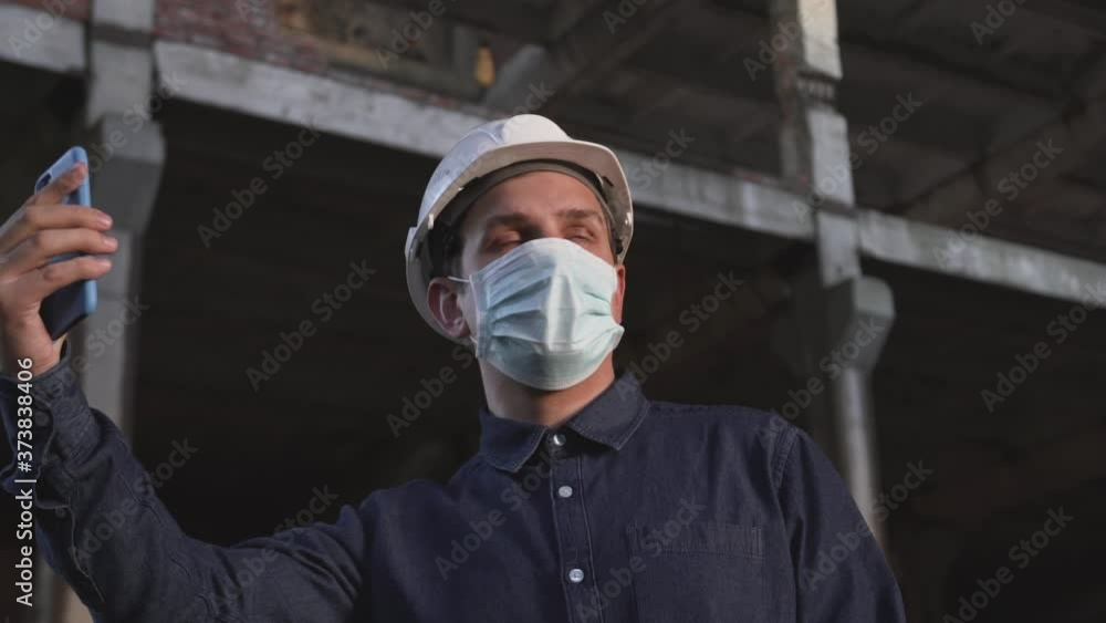 worker, foreman, builder, engineer, architect in dark shirt, white helmet, mask is at facility, at construction site, communicates via phone video communication, shows project, talks, reports on work worker, foreman, builder, engineer, architect in dark shirt, white helmet, mask is at facility, at construction site, communicates via phone video communication, shows project, talks, reports on work