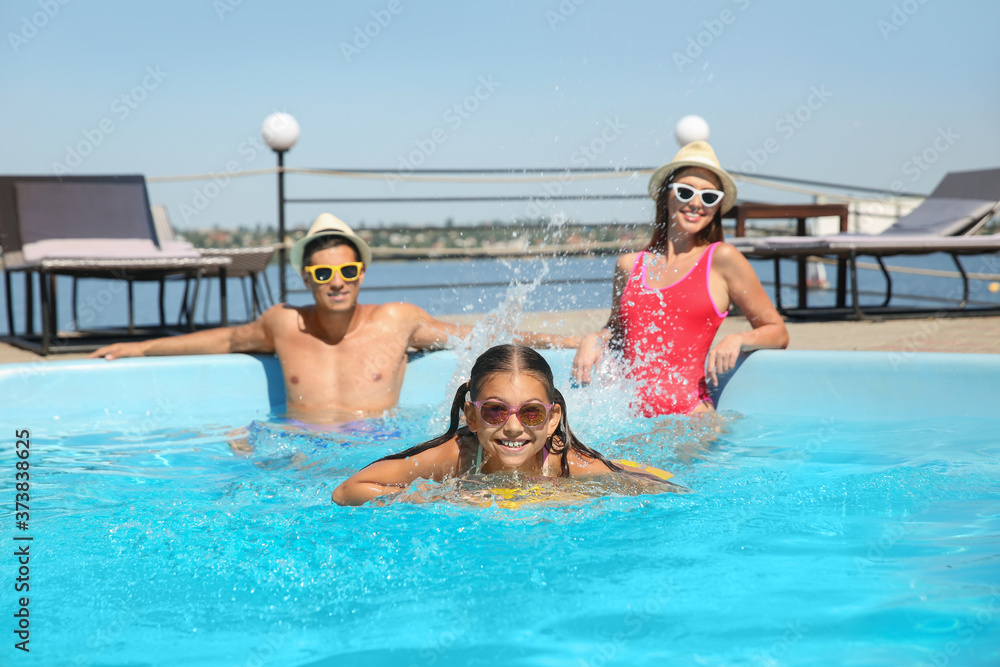 Happy girl and her parents having fun in swimming pool. Family vacation