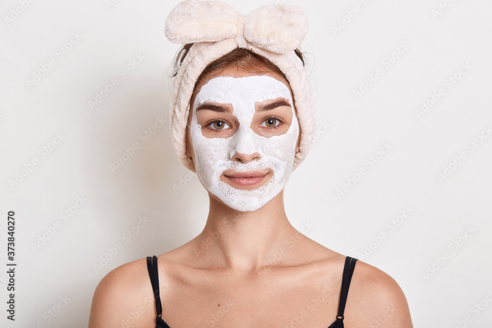 Portrait of beautiful girl with hairband her head applying facial mask, looking directly at camera with calm facial expression, doing cleansing procedures for her face skin. Portrait of beautiful girl with hairband her head applying facial mask, looking directly at camera with calm facial expression, doing cleansing procedures for her face skin.