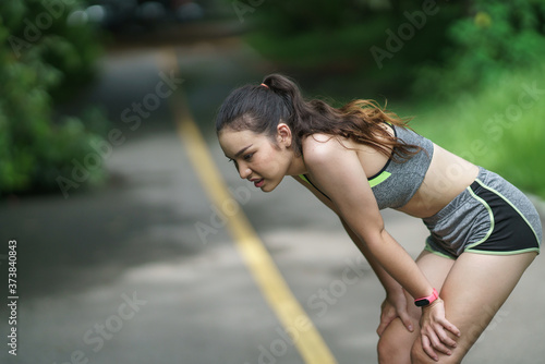 Tired female runner taking a break after running. Tired young athletic woman runner taking a rest, doing break, breathing hard after running hard.