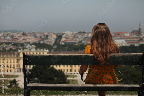 Unrecognizable girl sitting on a bench looking a city