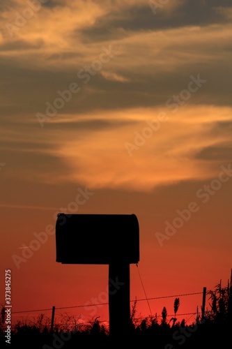 Country Mail Box silhouette out in the country with a colorful sky and clouds in Kansas north of Hutchinson Kansas USA.