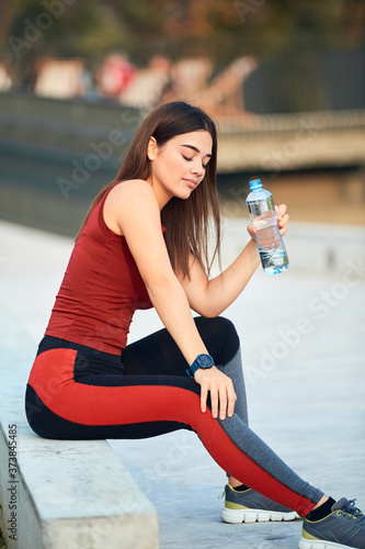 Thirsty young sporty woman making pause and drinking water during exerising. photo